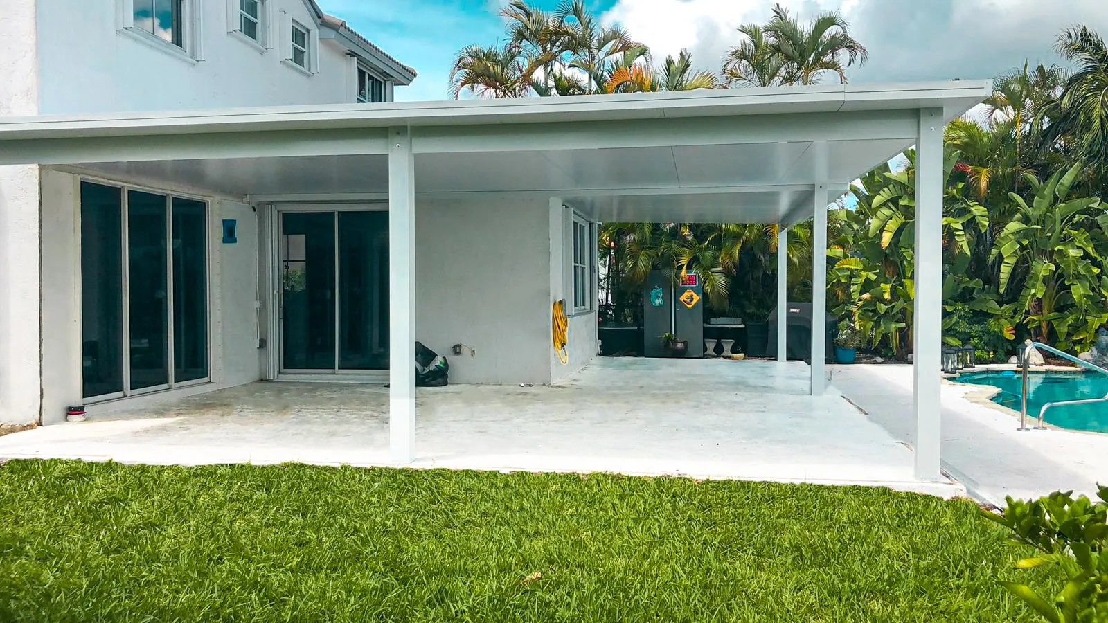 Wide white insulated aluminum patio cover across the back of a two-story white house beside a pool