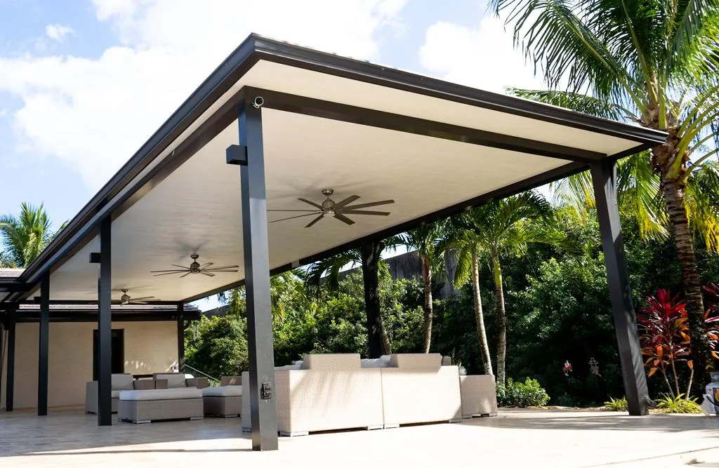 Large black-framed insulated patio cover with ceiling fans over cream wicker sofas surrounded by palms
