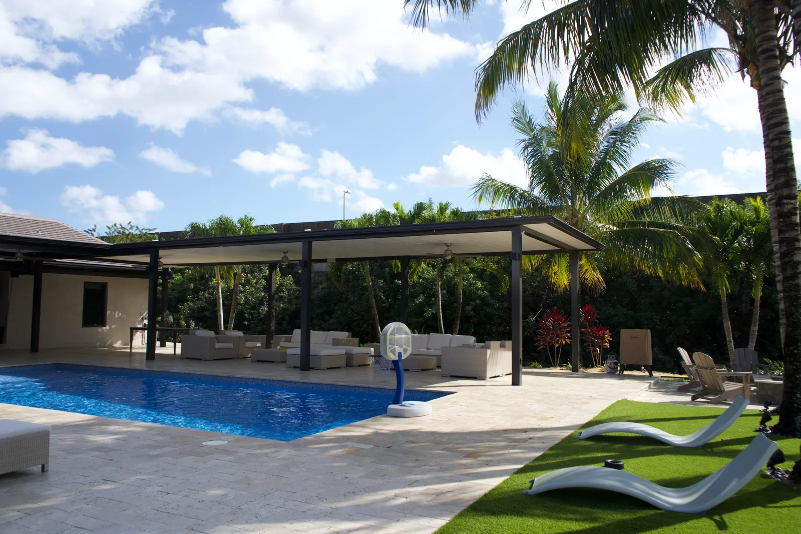 Long black-framed insulated patio cover with wicker lounge seating beside a lap pool and travertine deck