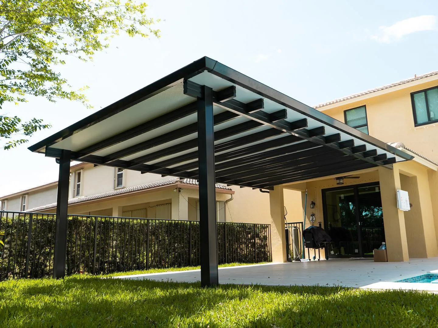Low-angle view of a black-framed insulated patio cover with square rafter tails on a yellow two-story home