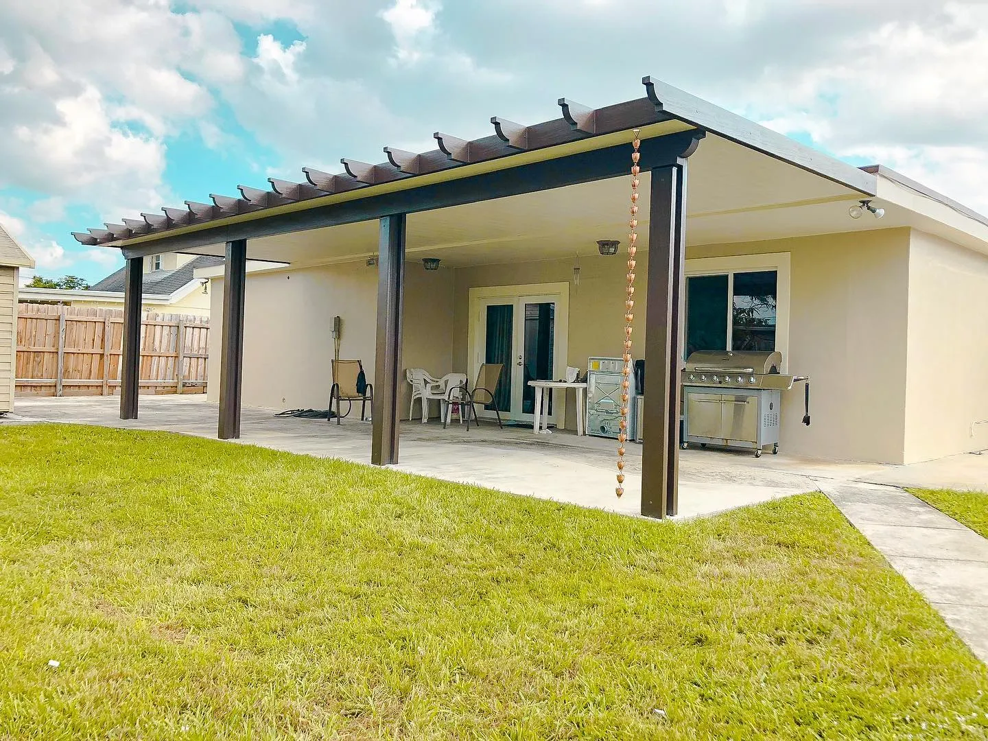 Brown insulated patio cover with decorative rafter tails and rain chain across the back of a one-story house