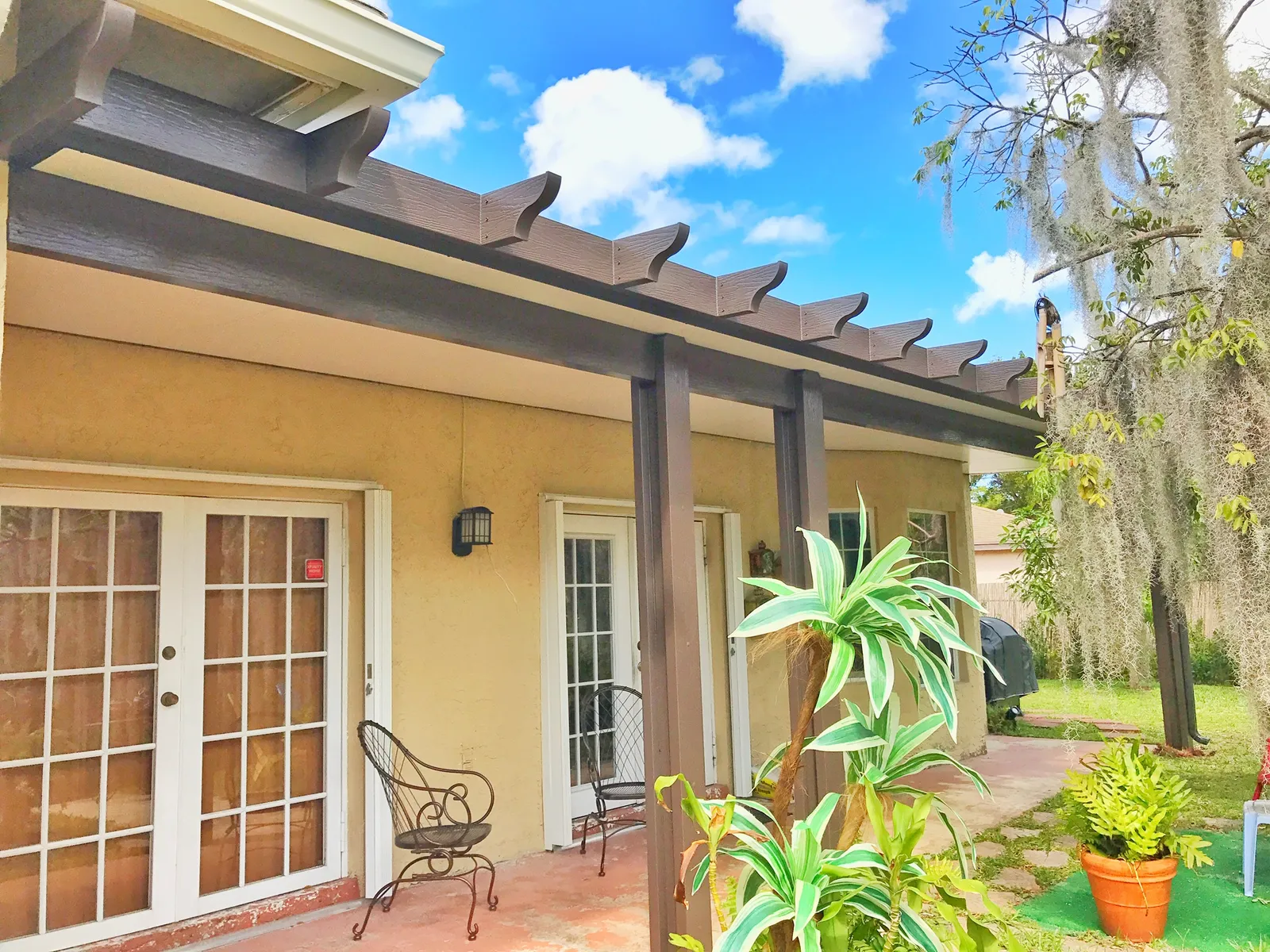 Brown insulated patio cover with scalloped rafter tails over French doors on a yellow stucco house