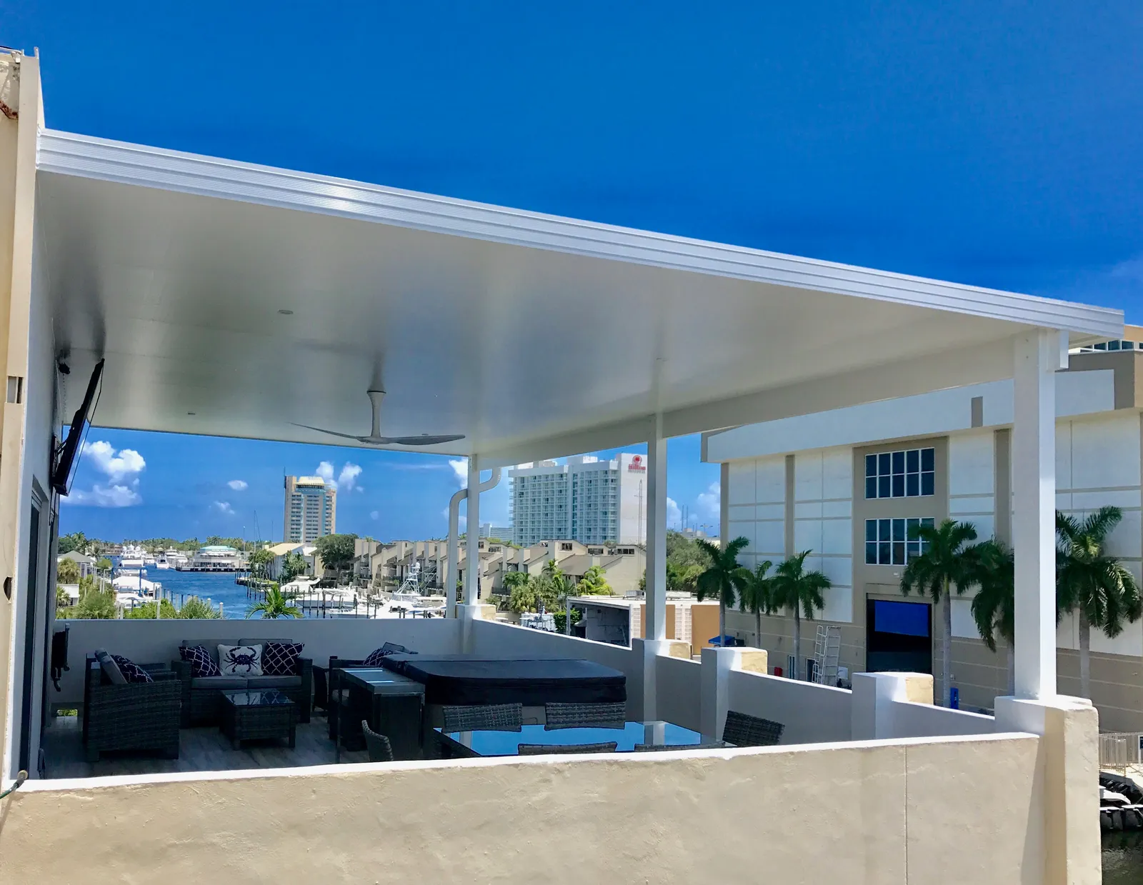 White insulated aluminum patio cover over a rooftop terrace with wicker seating and a marina view