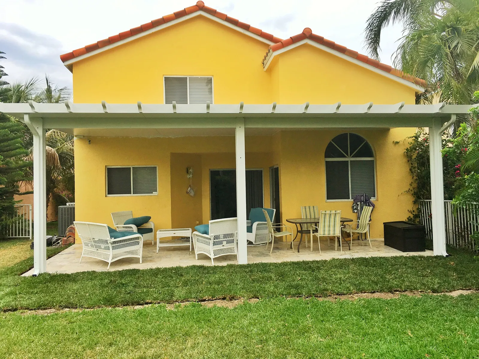 White insulated patio cover with rafter tails across the back of a yellow two-story house with tile roof