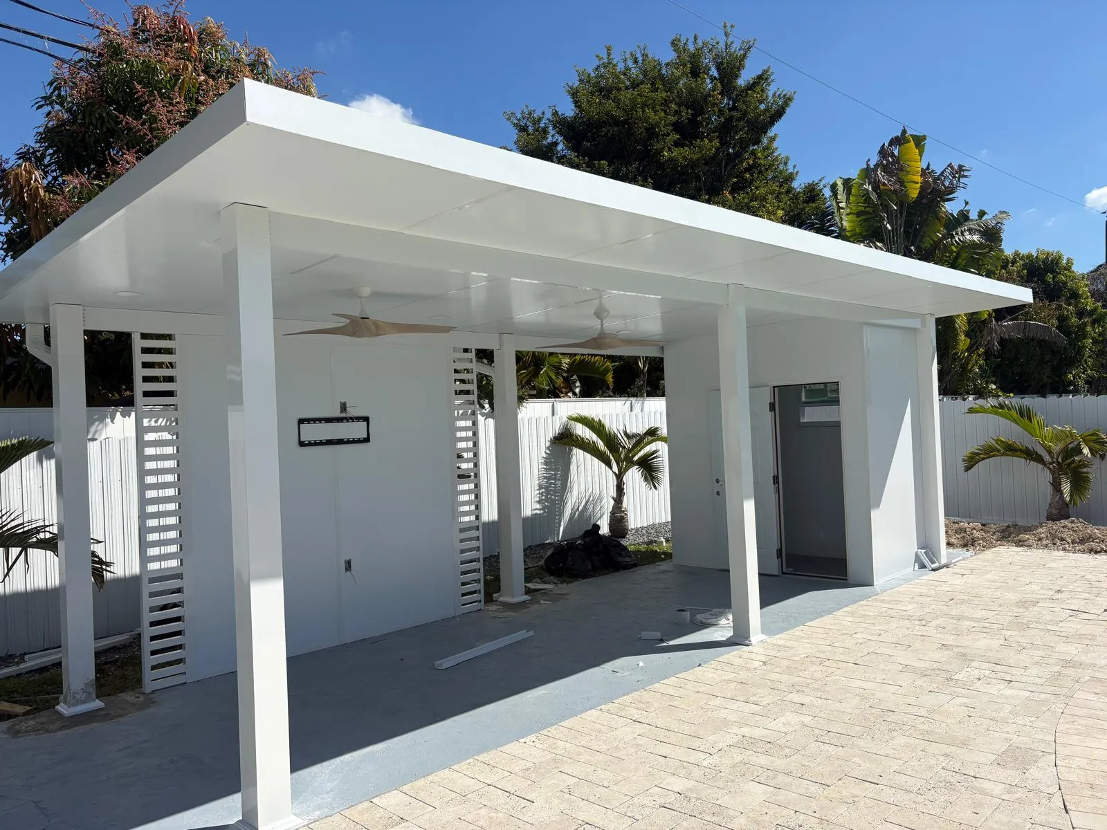 White flat-roof insulated patio cover with slatted side panels and ceiling fans beside a travertine paver patio