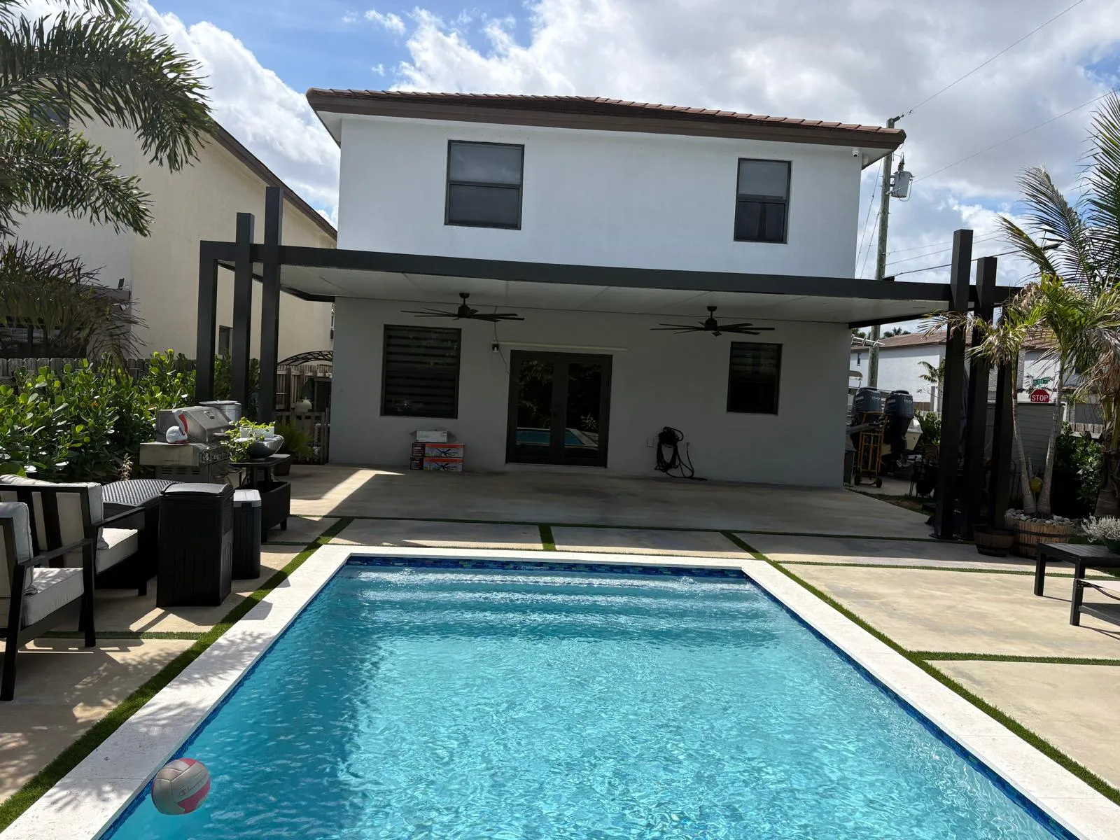 Black-framed flat patio cover across the back of a white two-story home seen over a rectangular pool