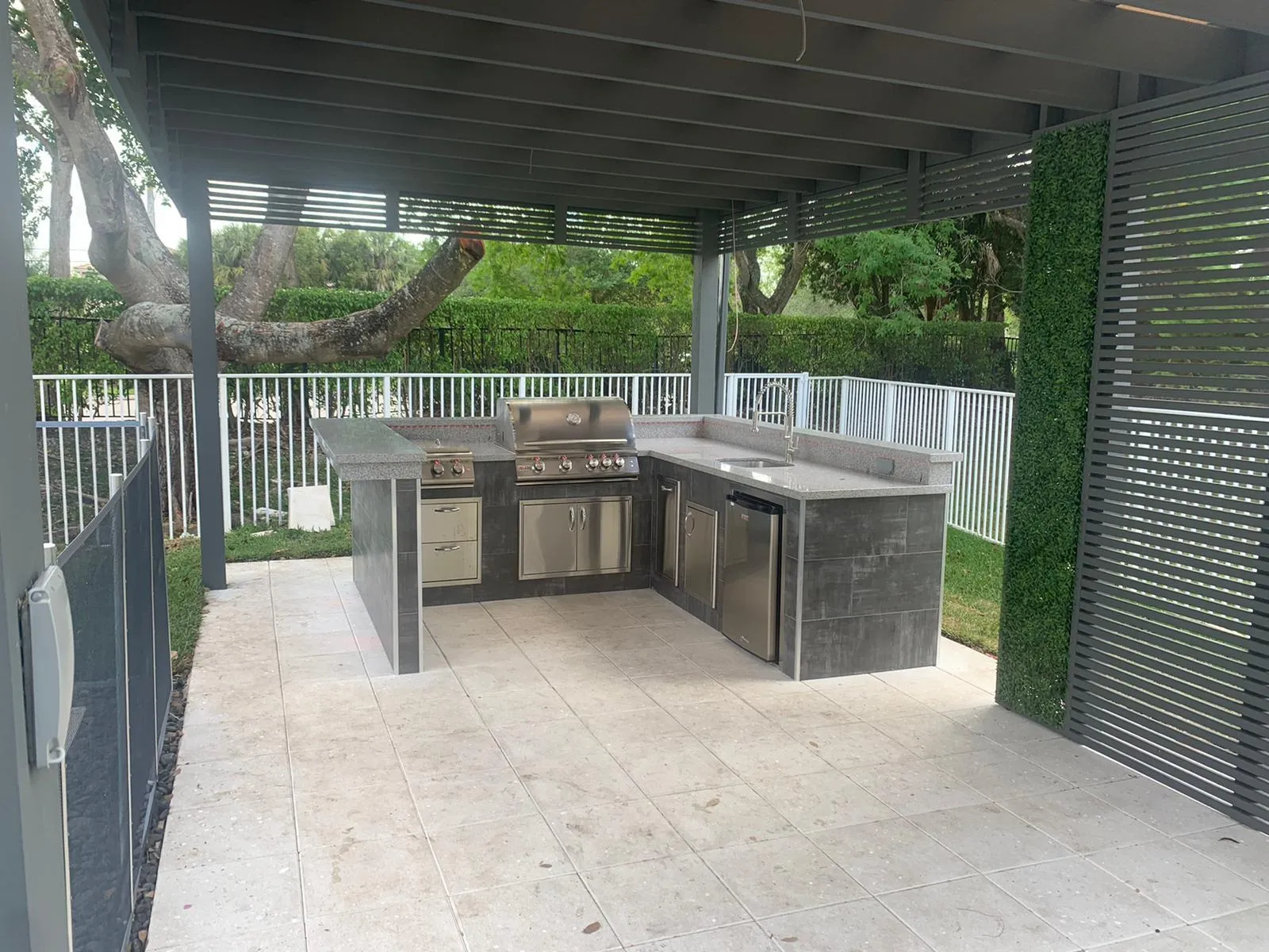 Gray aluminum pergola with slat privacy screen over a U-shaped tiled outdoor kitchen.