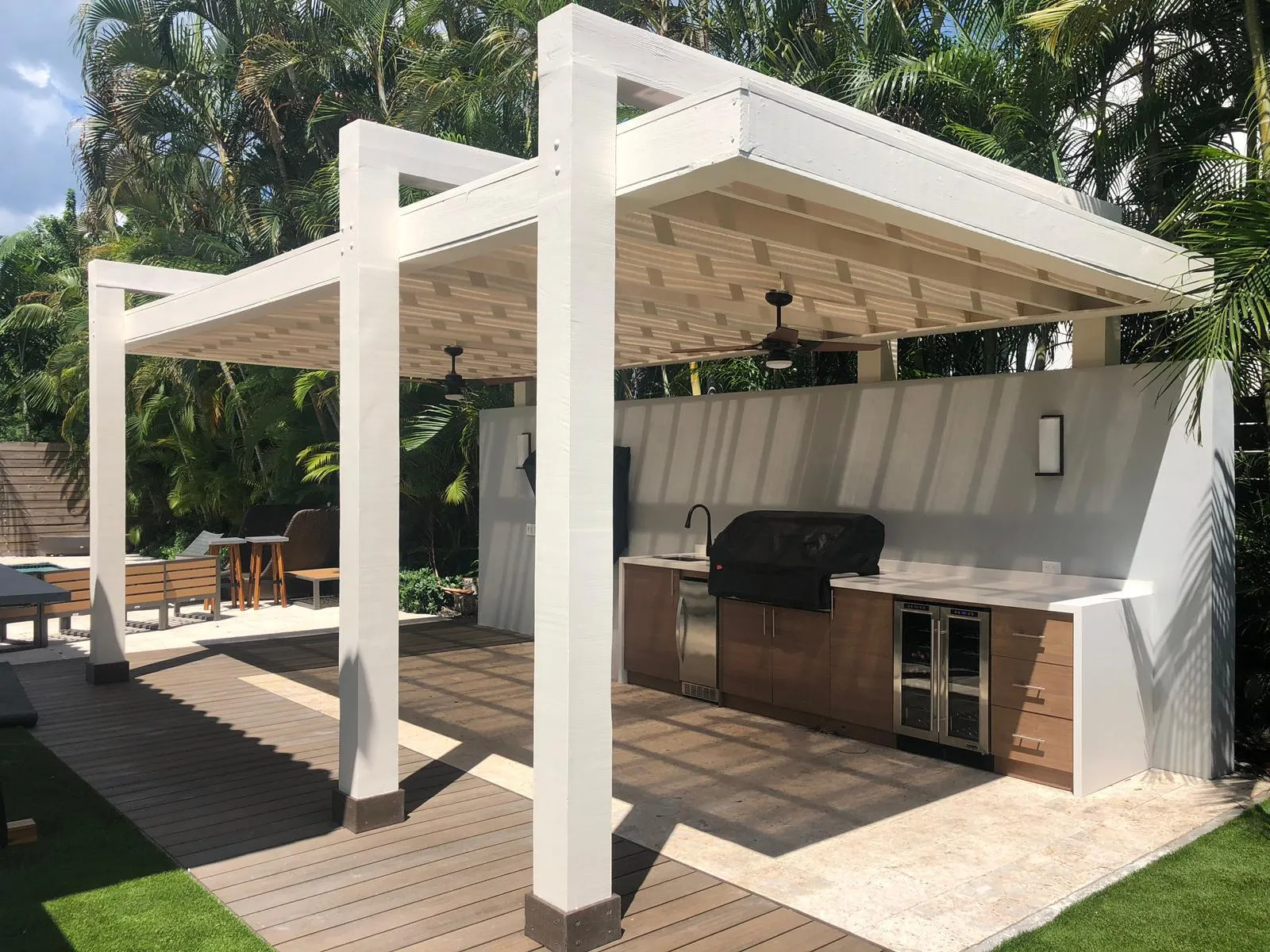 White pergola over an outdoor kitchen with wood-look cabinets and wine fridge on a composite deck.
