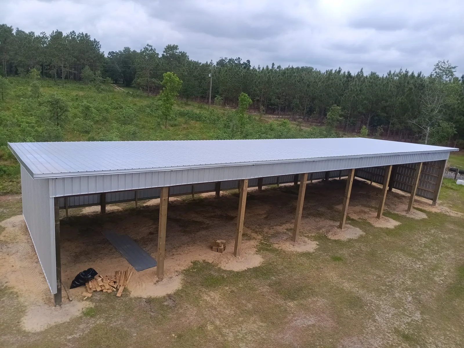 Aerial view of a long single-slope pole barn with galvanized metal roof and open front bays.