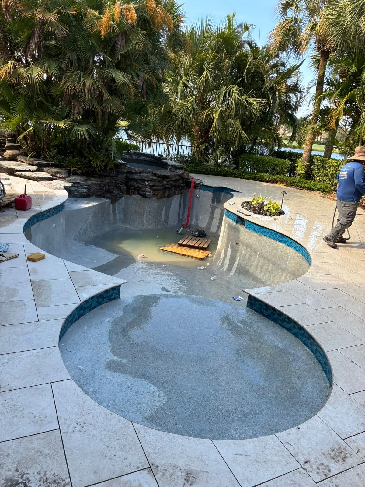 Drained freeform pool with new pebble finish, blue glass tile and rock waterfall spa.