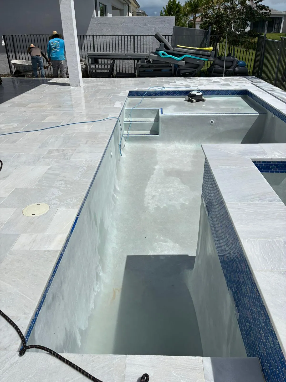 Empty pool with new plaster finish, blue glass waterline tile and white marble coping.