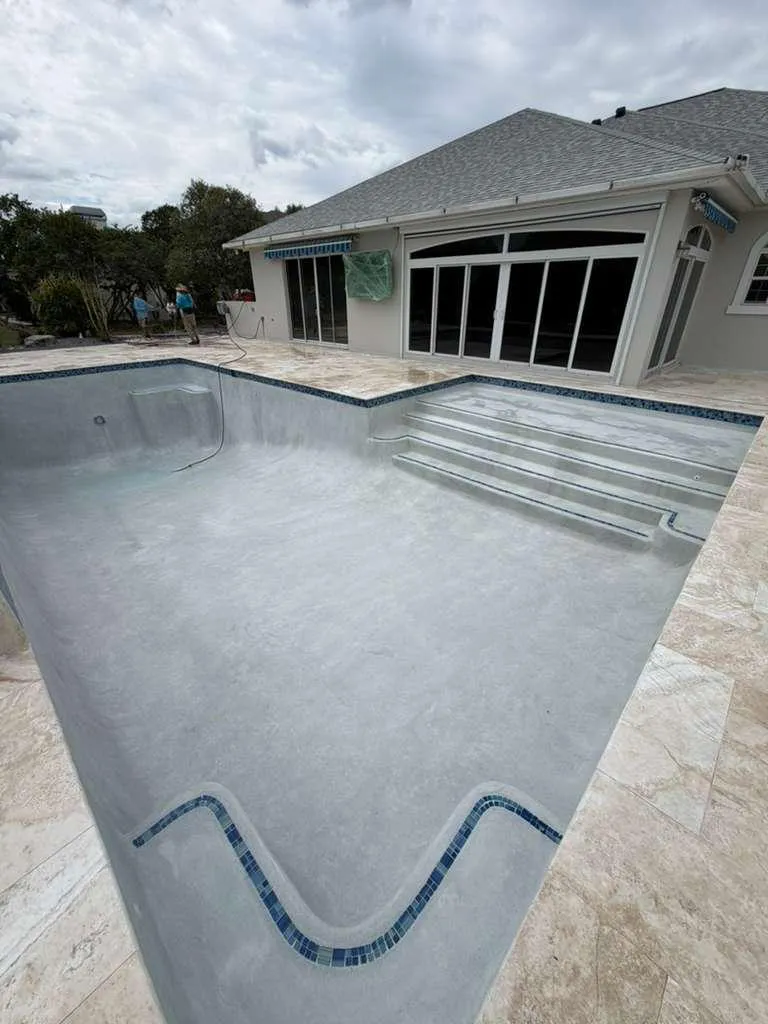 Freshly plastered pool with blue tile-trimmed steps and bench before filling.
