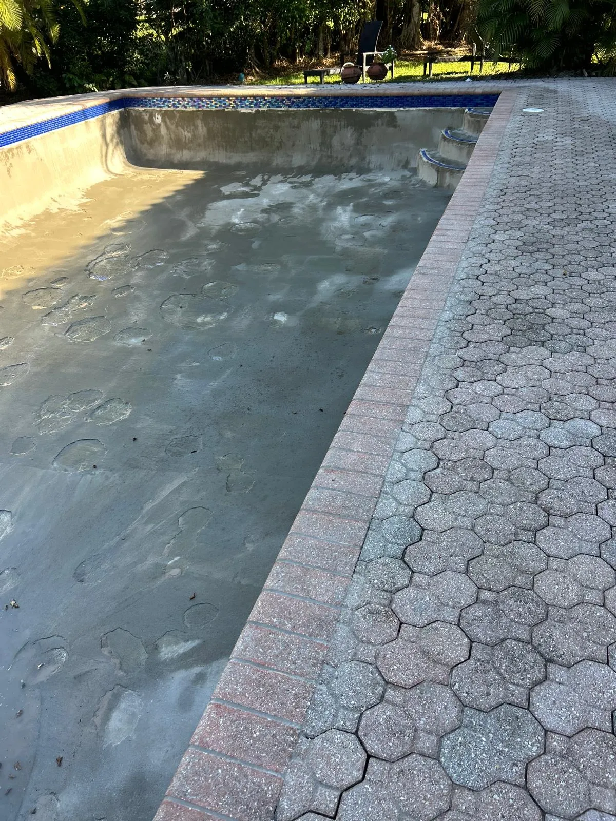 Pool shell with bond coat and new iridescent blue glass waterline tile beside an octagonal paver deck.