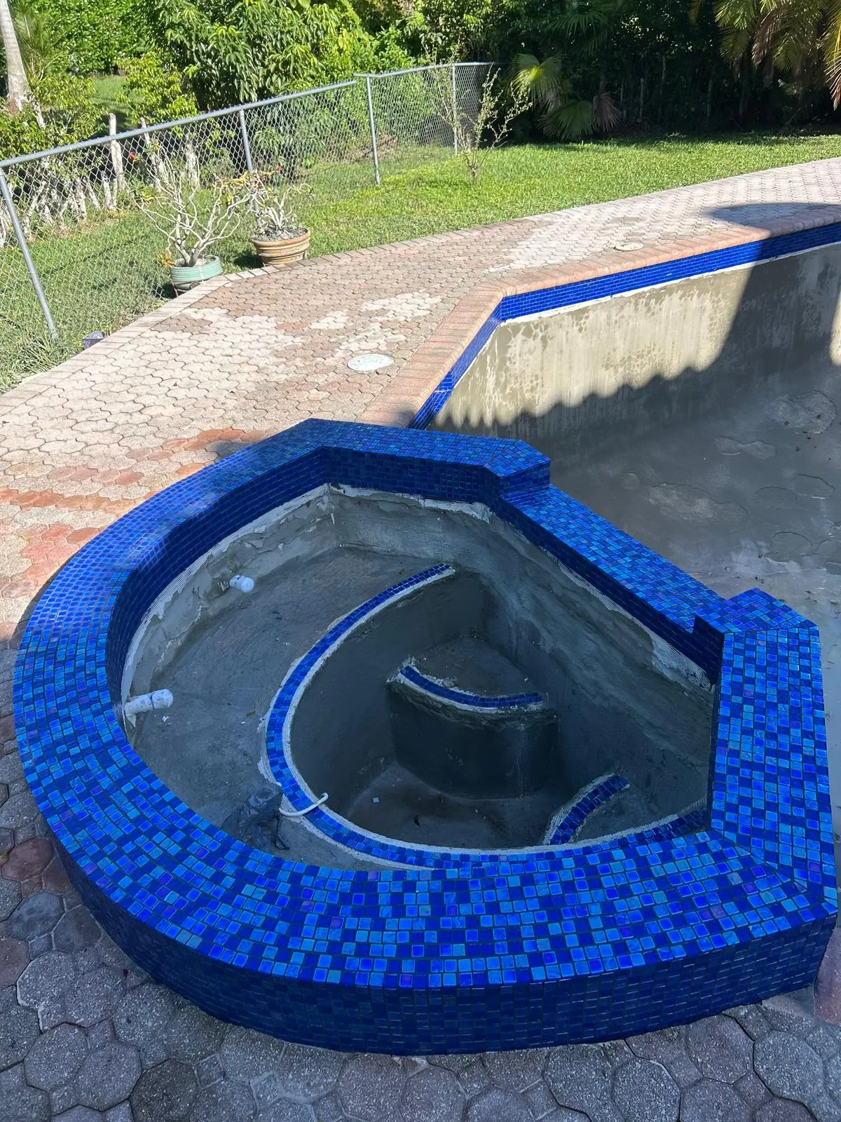 Top view of a raised spa with new iridescent blue glass mosaic on the rim and bench edges mid-remodel.