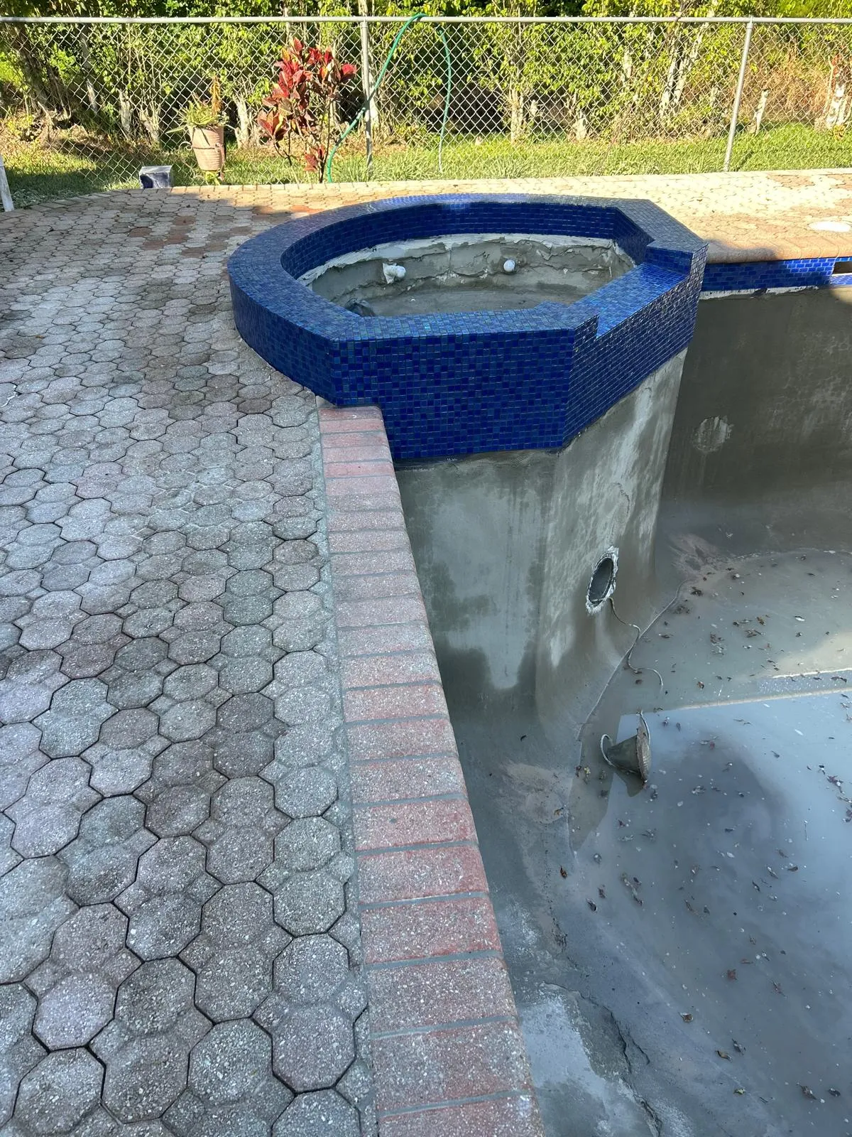 Raised spa freshly clad in blue glass mosaic tile during a pool remodel, with the pool shell drained.