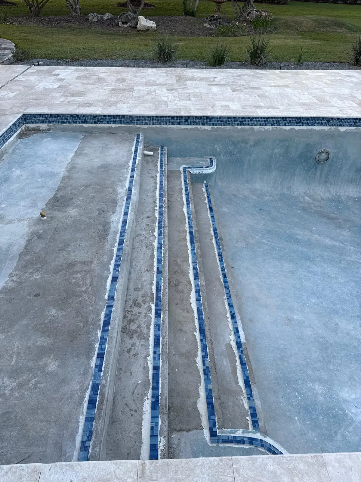 Pool steps and bench with new blue glass tile trim set before plaster, with the travertine deck above.