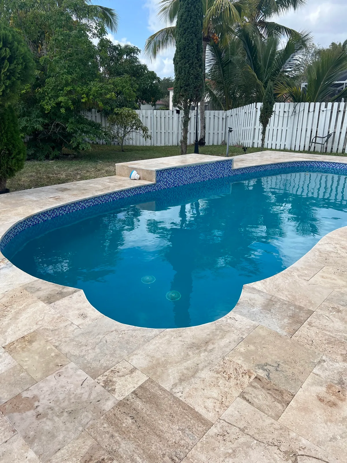 Remodeled freeform pool with blue mosaic waterline tile and travertine deck.