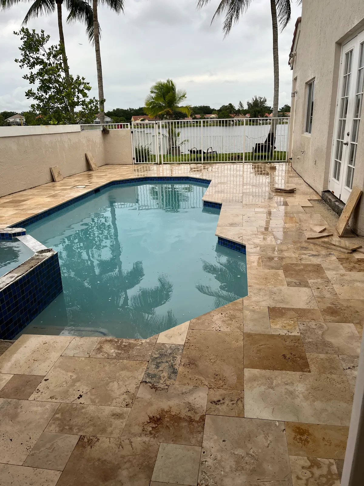 Pool with new wet travertine deck and blue tile overlooking a lake, work nearly done.