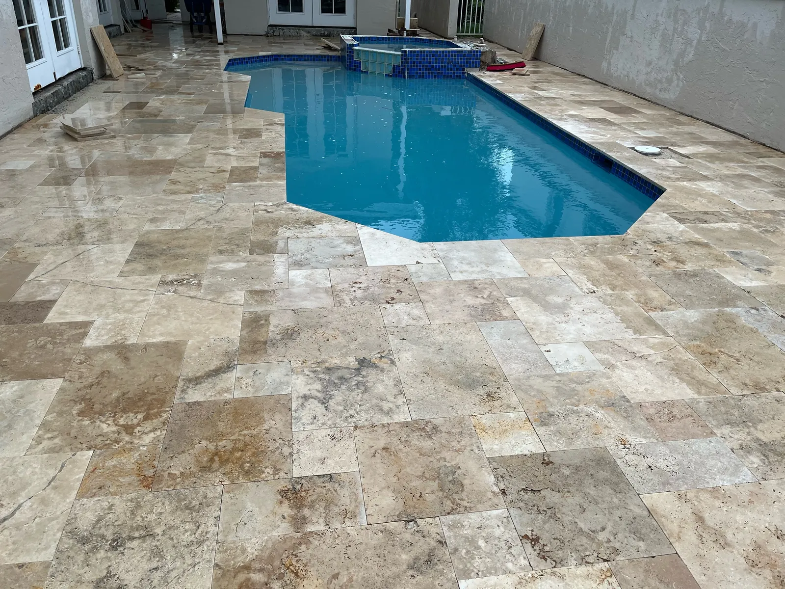 Walnut travertine deck in French pattern around a pool with a blue-tiled raised spa.