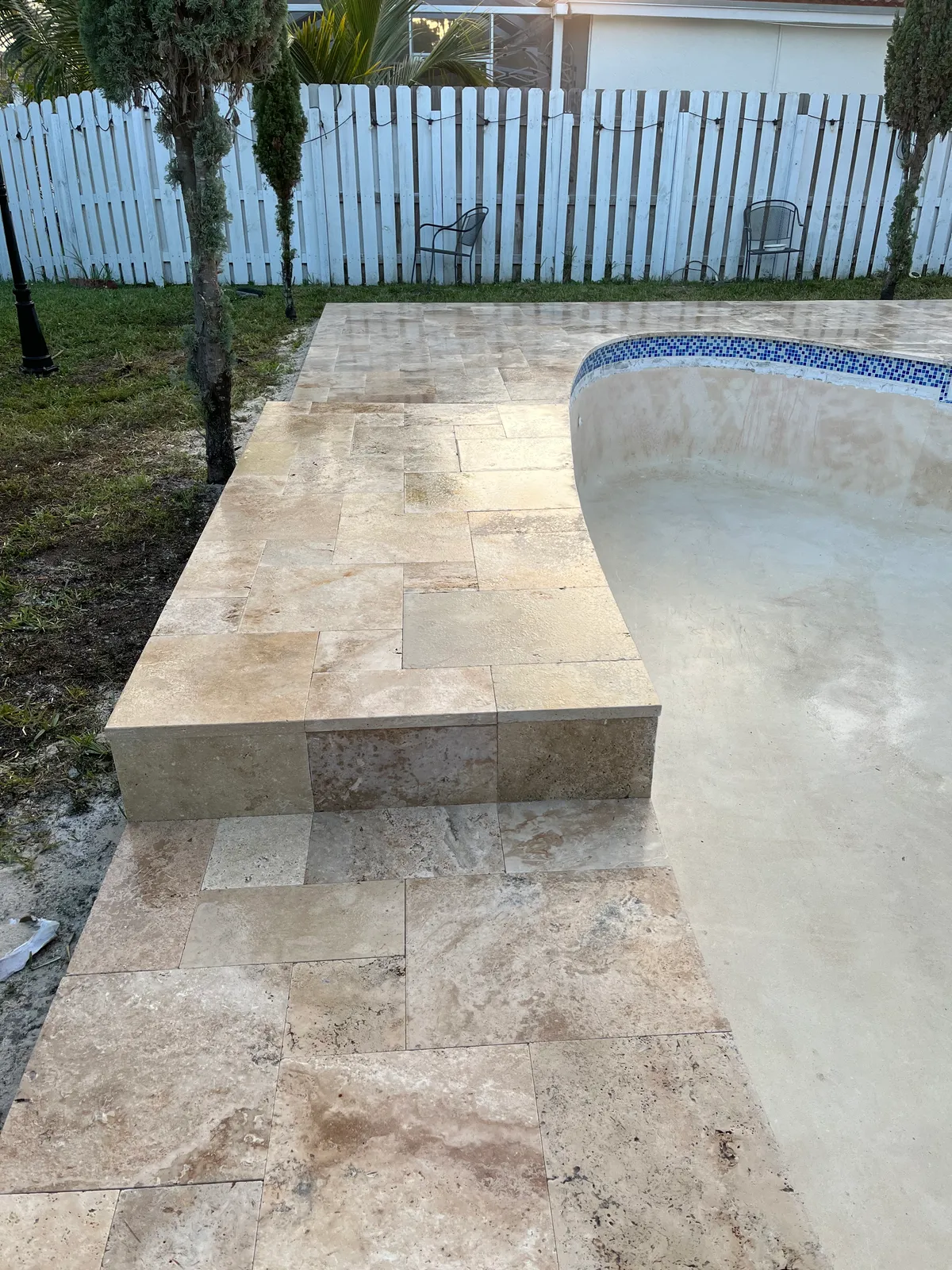 Drained kidney-shaped pool with new travertine deck, raised step and blue mosaic tile.