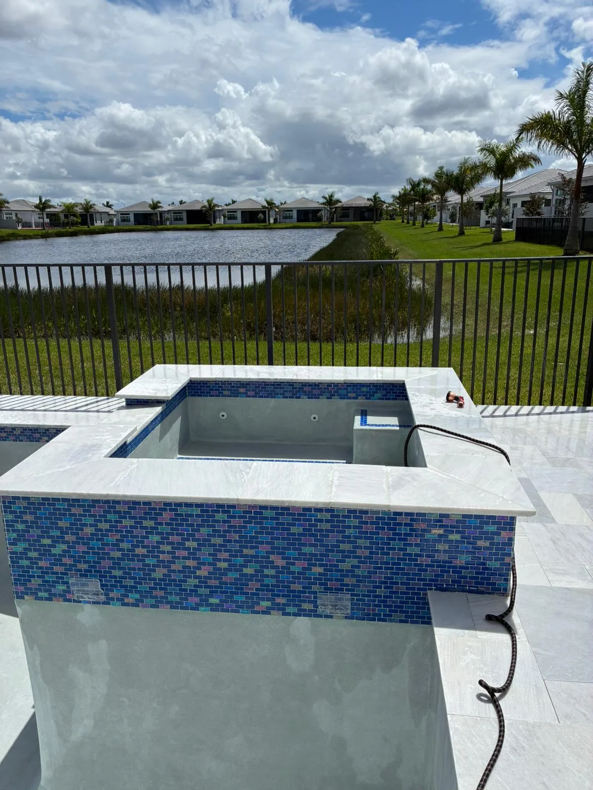 Raised spa with iridescent blue glass tile and white marble coping overlooking a lake.