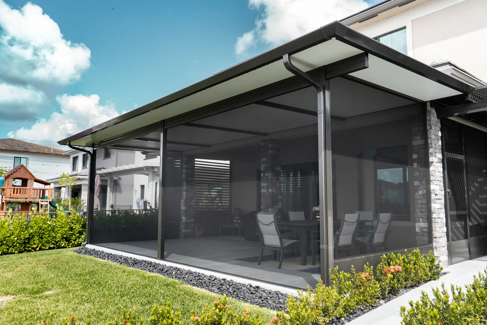Dark-framed patio screen room under an insulated roof, with a dining set seen through the mesh.