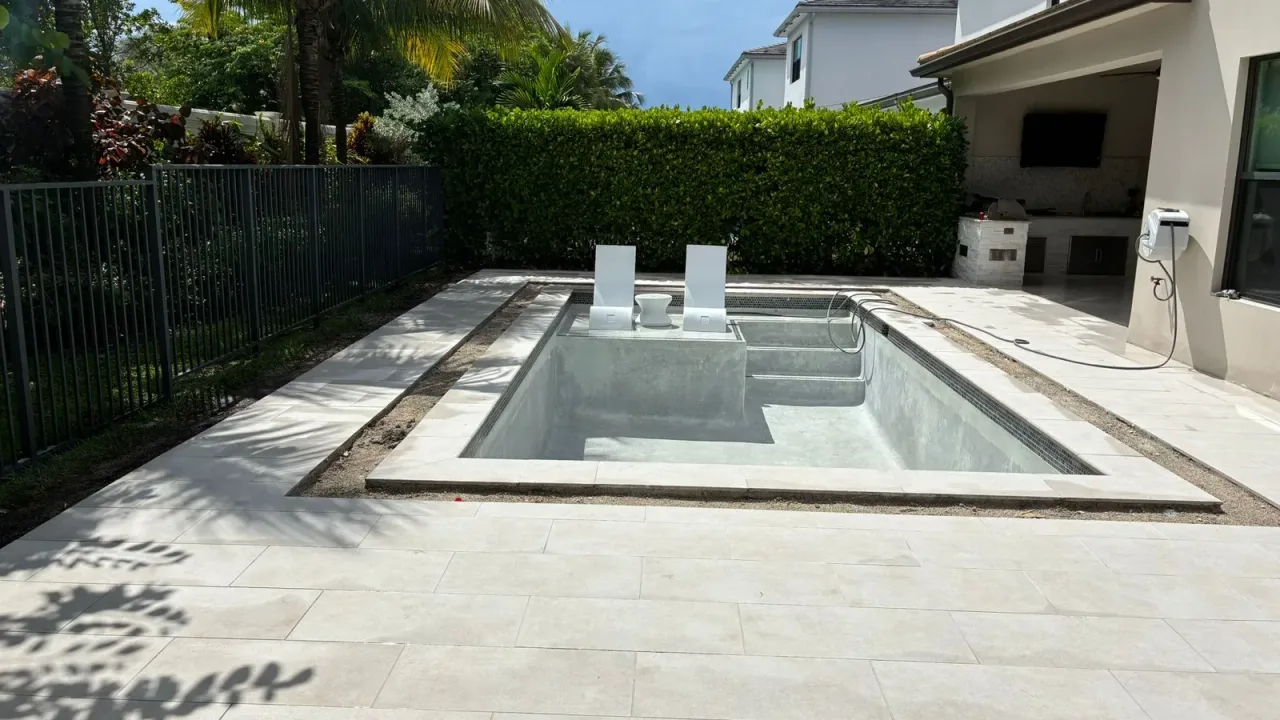 Empty new pool with two loungers on its sun shelf beside the entry steps, set in a deck of large-format pale tiles.