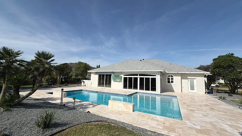 Rectangular pool with a raised travertine water-feature wall and a wide travertine deck behind a single-storey house