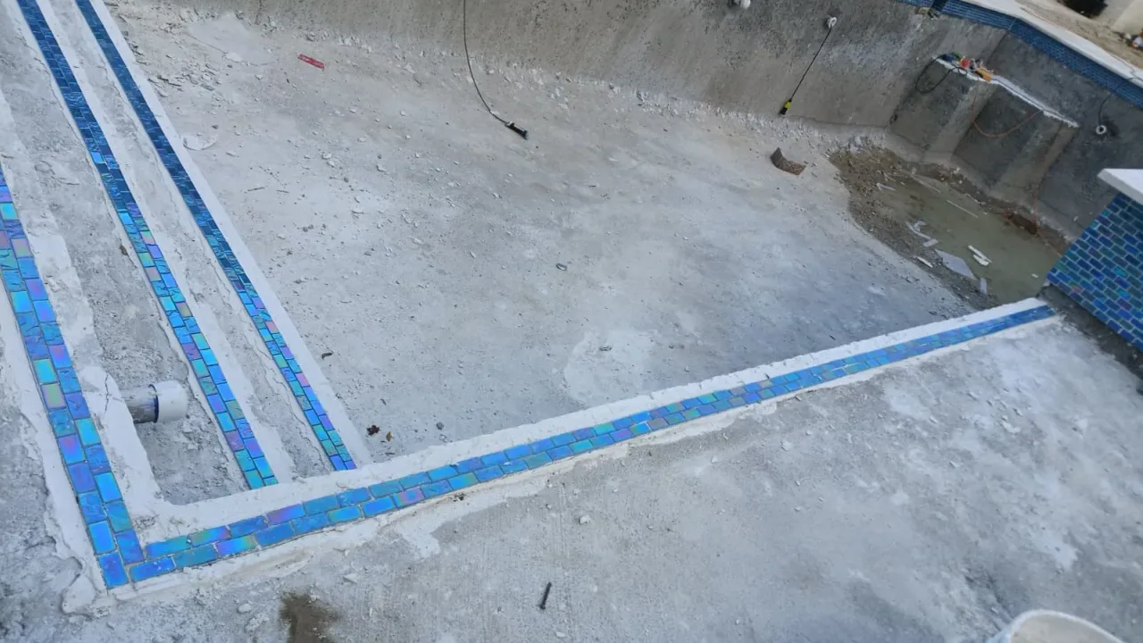 Iridescent blue glass tile outlining the steps and sun shelf of a pool shell before plaster.
