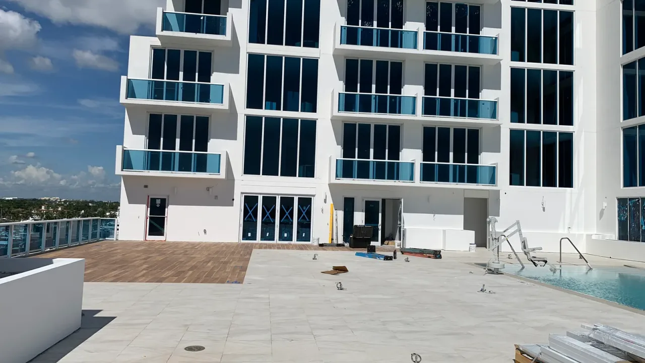 Pool deck below a white multi-storey tower, with a pool lift and a handrail at the water's edge.
