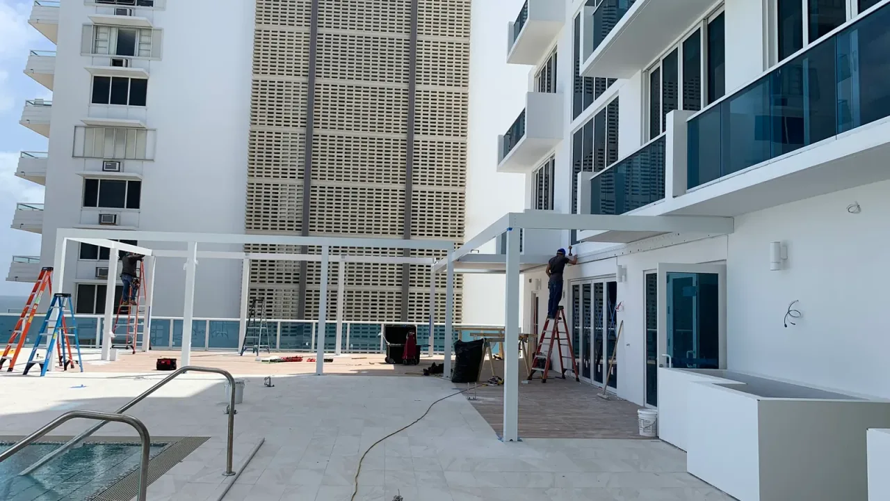 Pool steps with twin handrails on a terrace between residential towers, with white pergola frames going up.