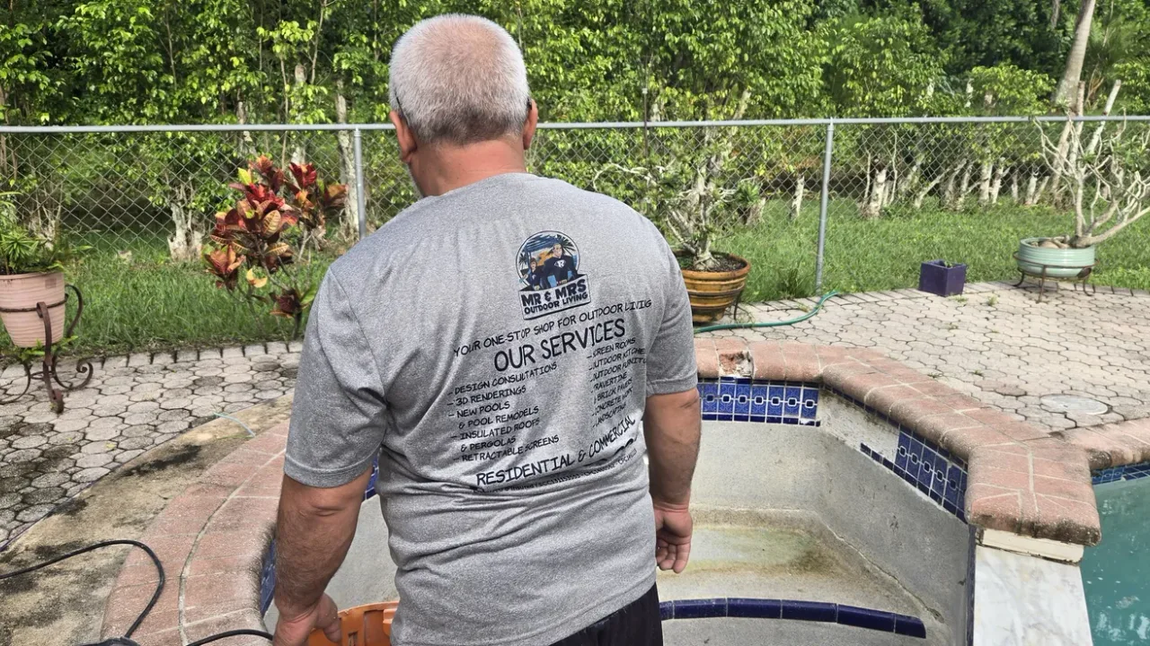 Crew member in a company shirt, seen from behind, looking into an old tiled spa beside a pool.