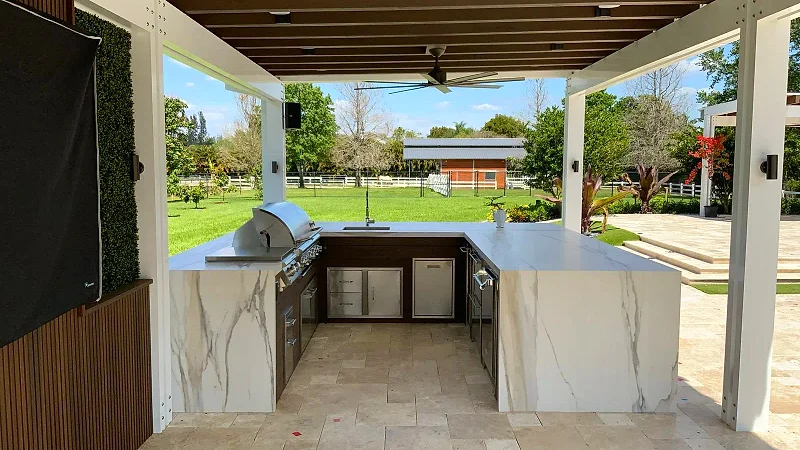 U-shaped outdoor kitchen with marble-look waterfall counters and a built-in grill under a white and wood pergola