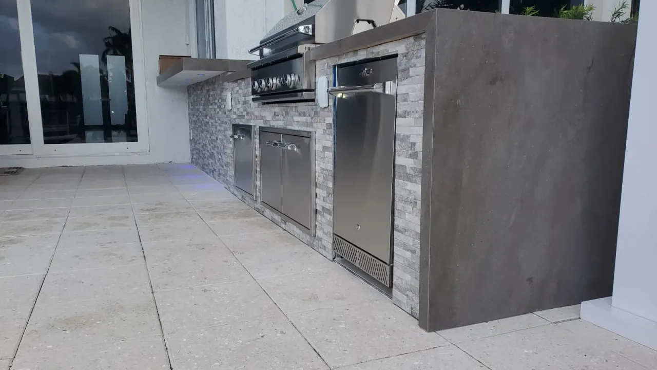 Gray stacked-stone outdoor kitchen run meeting a smooth gray slab end panel at the outside corner, with stainless doors.