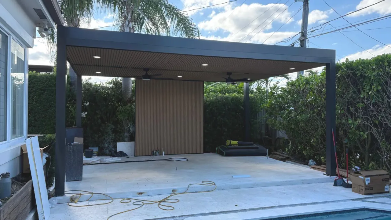 Black-framed cover with a wood-look slat ceiling, recessed lights and two fans, cords and boxes still on the slab by a pool