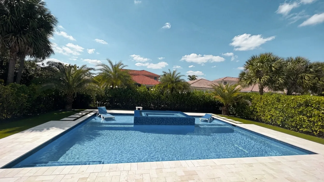 Rectangular pool with a raised spa and water spouts, set in a herringbone travertine deck.