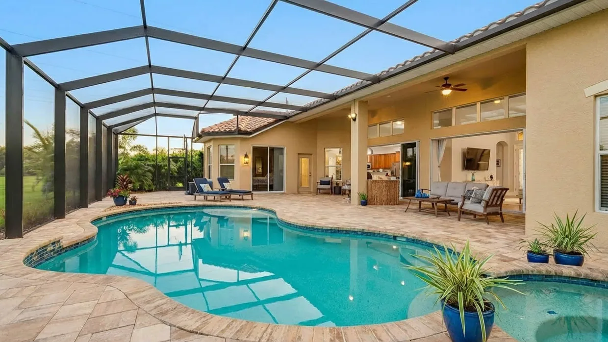 Freeform pool inside a dark-framed screen enclosure that joins the house at a covered lanai with a ceiling fan.