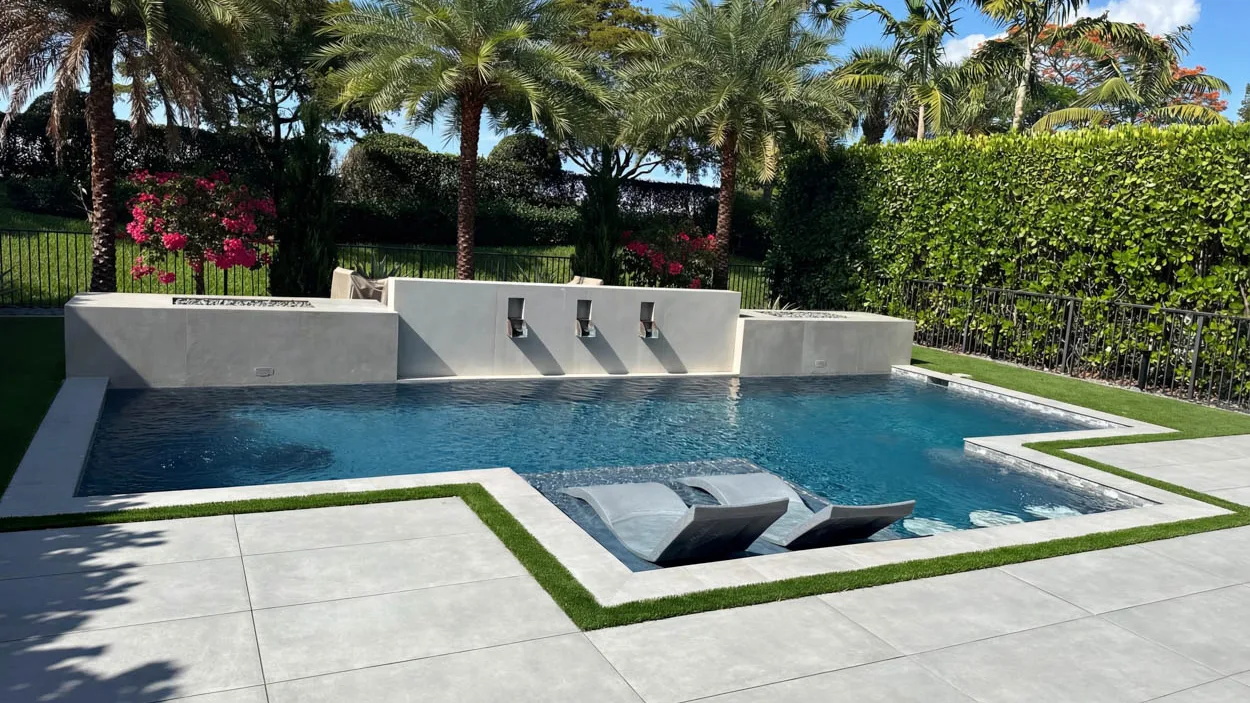 Rectangular pool with three spillway scuppers set into a rendered wall, a fire bowl on the deck and bougainvillea behind it.