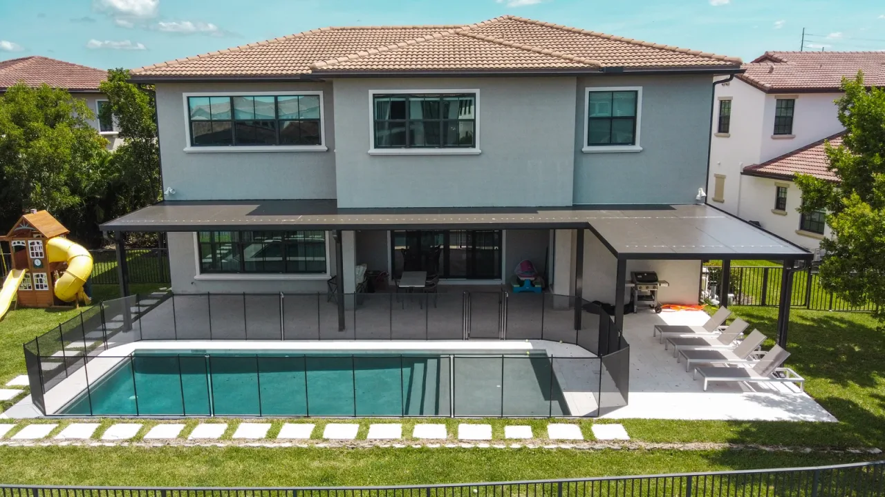 Lap pool seen from above, with a dark-framed aluminium patio cover running along the rear of the building.