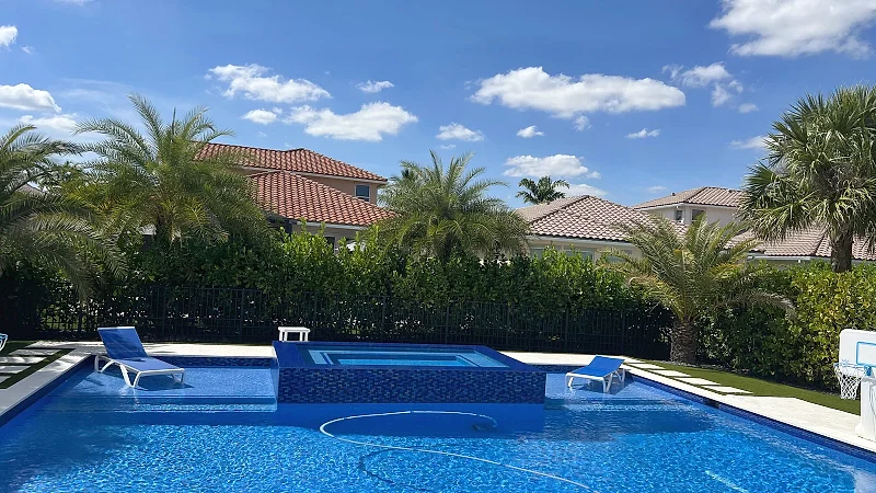 Remodelled rectangular pool with a raised spa clad in deep-blue mosaic, a pale travertine deck and a poolside basketball hoop.