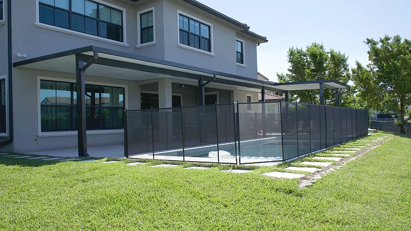 Lap pool behind a Florida home, enclosed by a removable black mesh safety fence, with a dark-framed aluminium patio cover over the lanai.