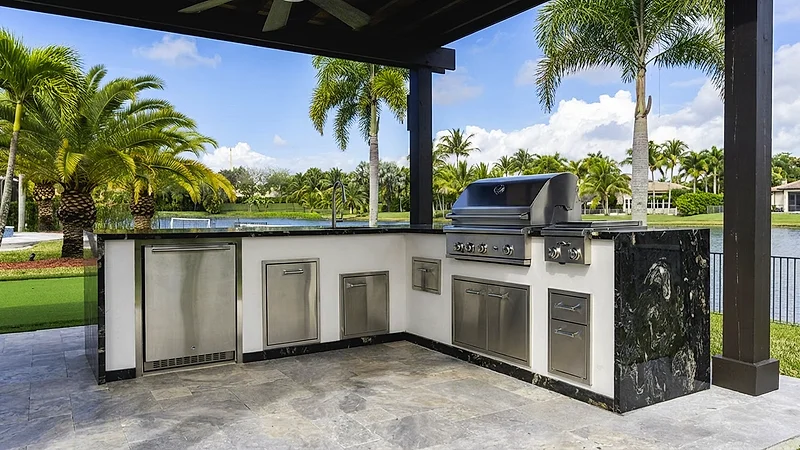 Poolside outdoor kitchen with a built-in grill and stainless cabinetry under a covered patio.