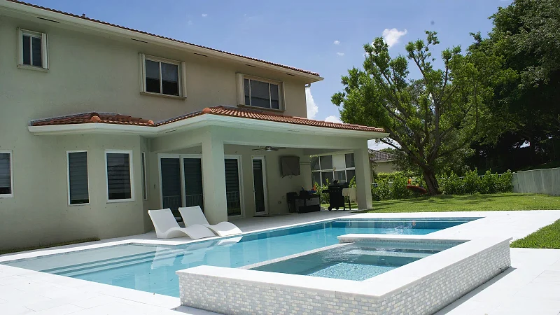 Finished pool and raised spa alongside the rear of the house, with loungers on the stone deck.