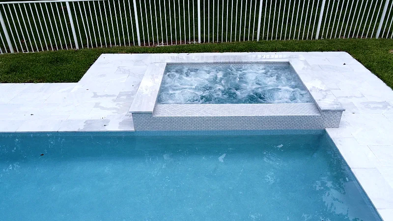 Aerial view of a rectangular backyard pool with a raised spa and a wide stone deck.