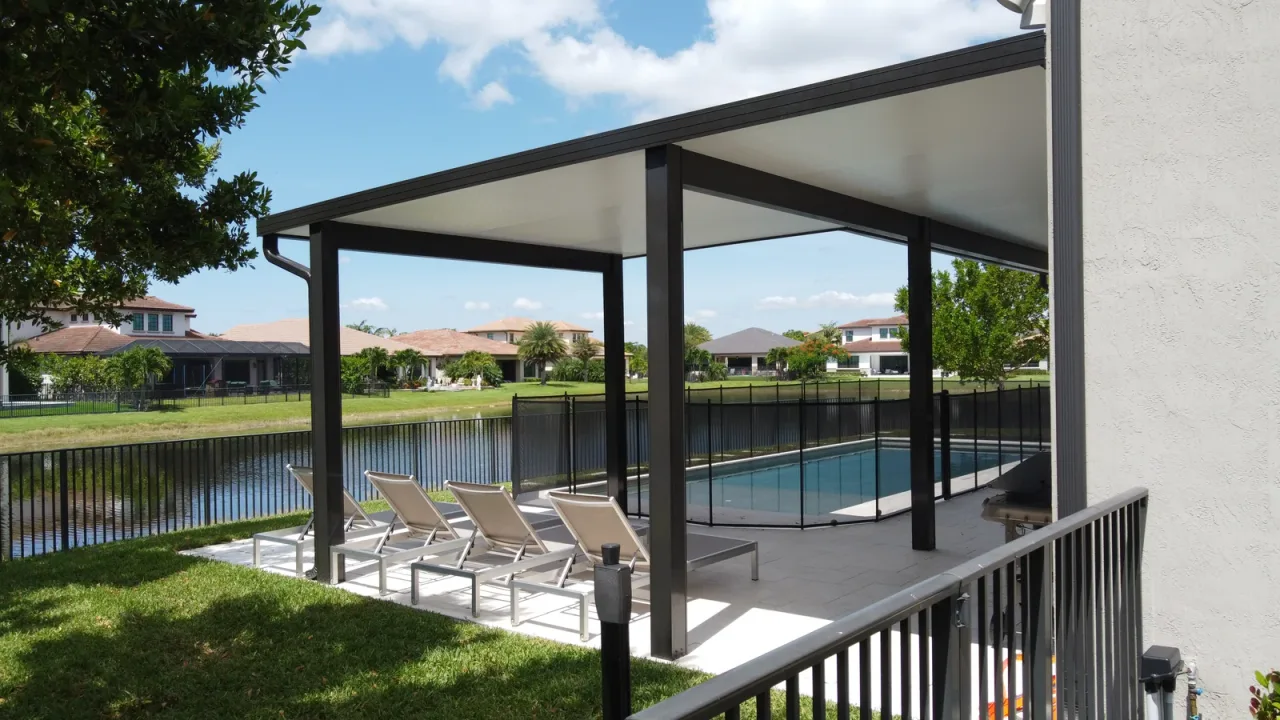 Long lap pool from above, set in a lawn beside a covered lanai and a lake.
