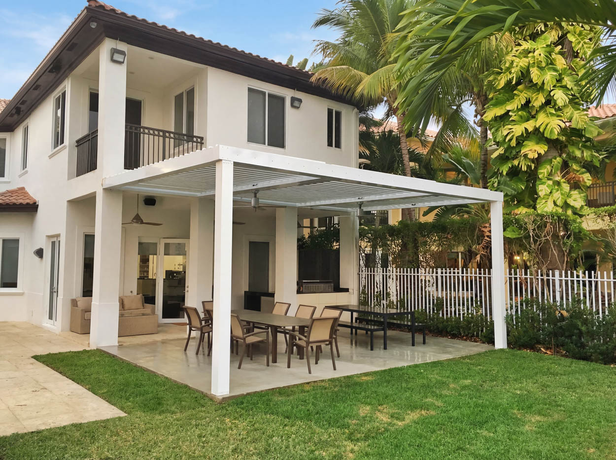 White motorized louvered roof system covering outdoor dining area, designed for sun control and modern backyard living in Florida.