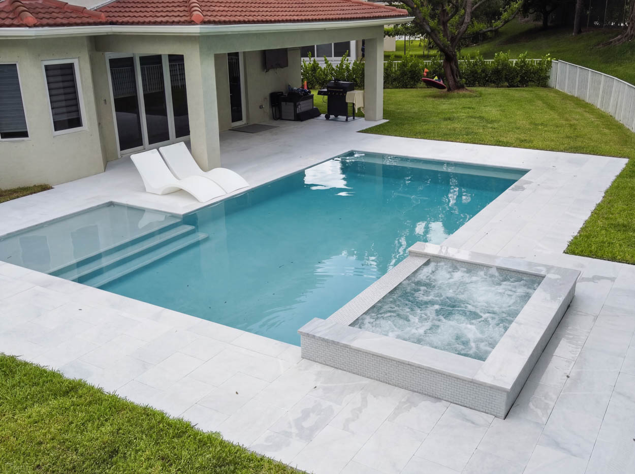 Luxury backyard pool and spa installation in South Florida featuring custom tile, palm landscaping and clean architectural lines.