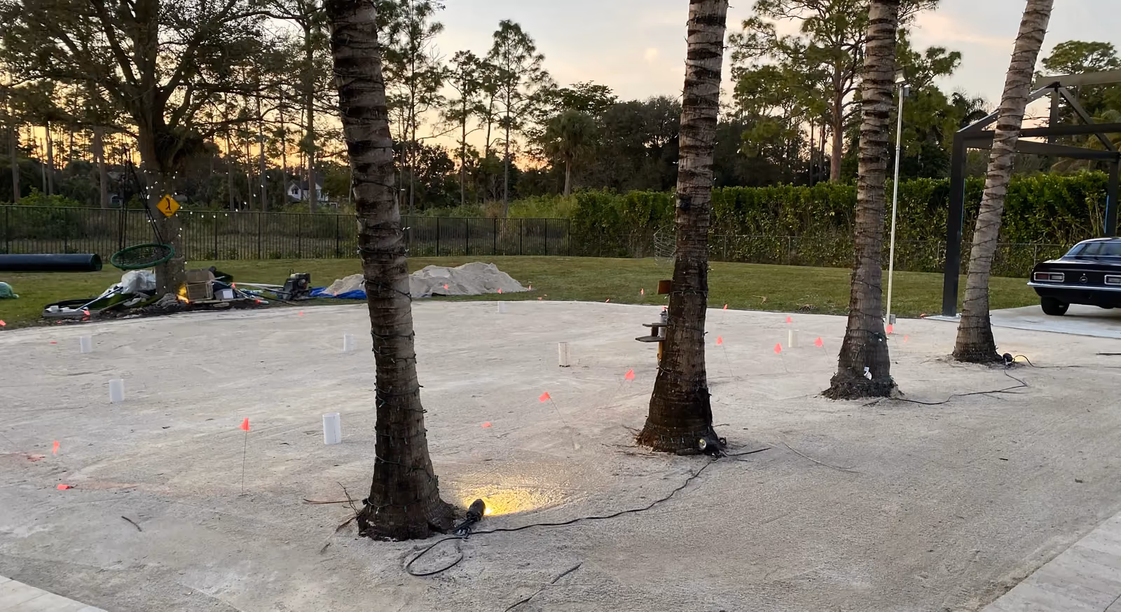 Compacted sand base with marker flags and sleeves around palm trees, ready for turf installation.