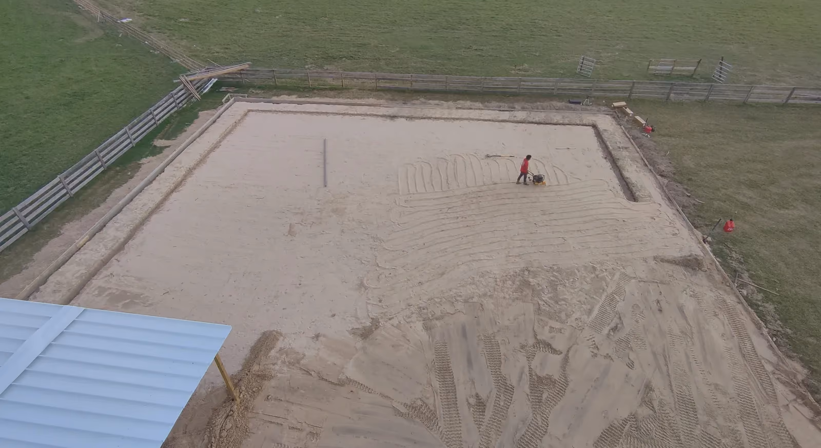 Aerial view of a worker compacting a sand pad for a concrete slab on a fenced ranch.