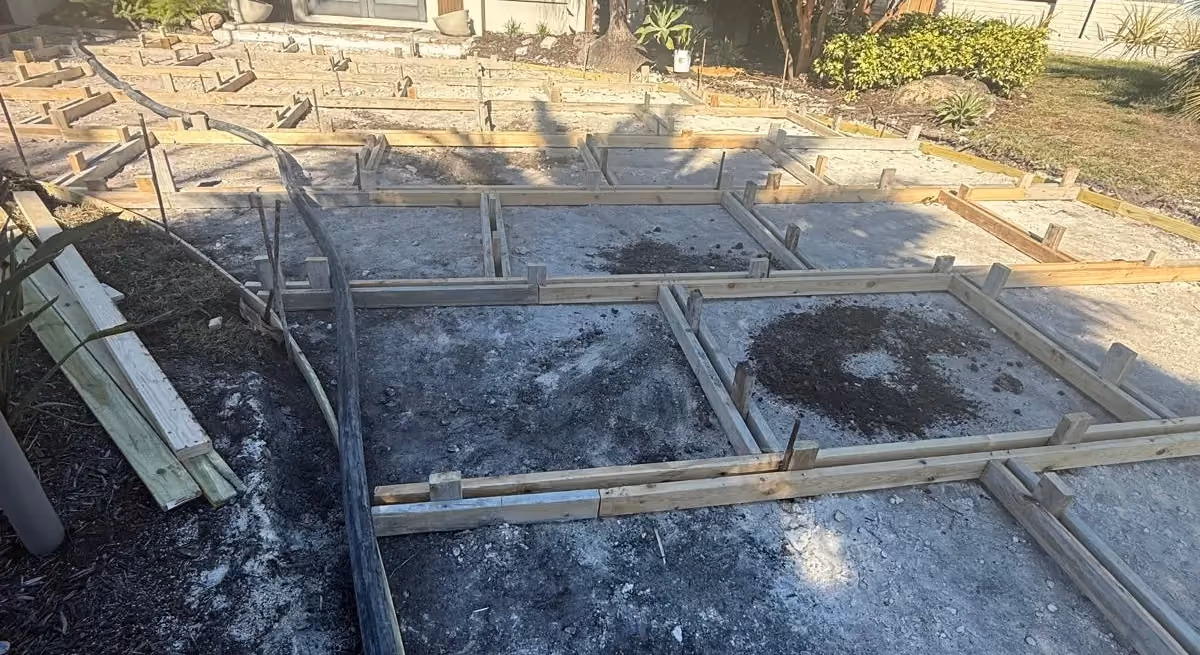 Wood formwork grid laid out for large concrete driveway slabs in front of a tile-roof house.